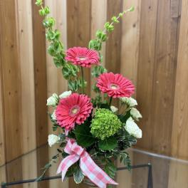 Everyday arrangement with pink gerbera daisies, green hydrangea, and white blooms in a glass vase with a pink bow.