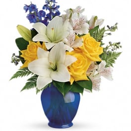 Bouquet of white lilies, yellow roses, and blue flowers in a blue vase