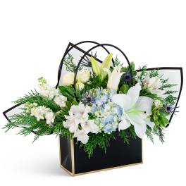 White lilies, roses, and blue hydrangea in a black gift bag
