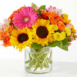Bright mixed bouquet with sunflowers, roses, and a pink gerbera in a glass vase