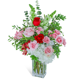Pink and red roses with white blooms in a clear square vase