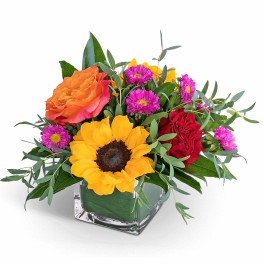 Mixed bouquet with sunflowers, roses, and purple daisies in a glass vase