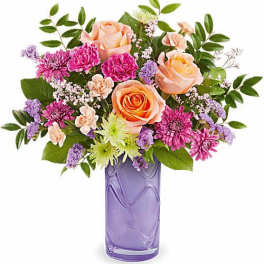 Peach roses and purple flowers in a lavender glass vase