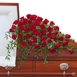 Red rose casket spray with cascading greenery on a wooden casket