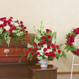 Red and white funeral floral set with casket spray, standing wreath, and tall urn arrangement