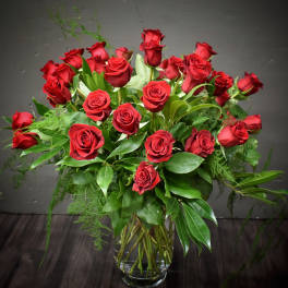Tall arrangement of long-stemmed red roses with lush foliage in a clear glass vase