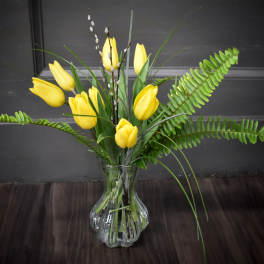 Yellow tulips arranged in a clear glass vase with fern fronds