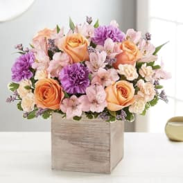 Bouquet of peach roses, pink flowers, and purple carnations in a wooden box