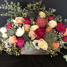 Low floral arrangement with roses, protea, and succulents in a wooden box
