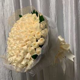Large hand-tied bouquet of cream roses wrapped in white mesh with an ivory ribbon bow