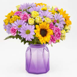 Mixed bouquet of sunflowers, daisies, roses, and carnations in a purple vase