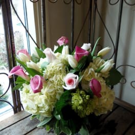 Pink calla lilies and white tulips arranged with pale hydrangeas in a glass vase.
