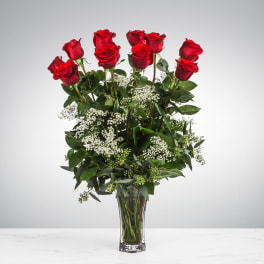 Tall bouquet of red roses and white filler flowers in a clear glass vase.