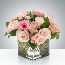 Low arrangement of pale pink roses and gerberas in a clear glass cube vase