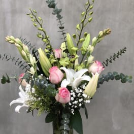 Tall bouquet of pink roses, white lilies, and green orchids in a glass vase