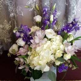 White and purple floral arrangement in a square container