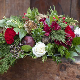 Holiday floral arrangement with red blooms and a white rose in a wooden box