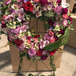 Heart-shaped floral wreath with pink, purple, and red flowers on a stand