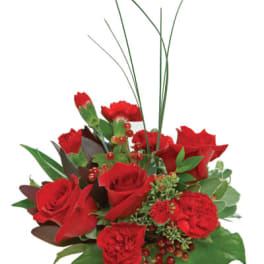 Compact red rose and carnation arrangement with berries in a clear glass cube vase