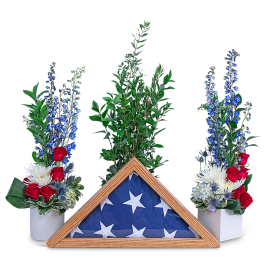 Red, white, and blue floral tribute with a folded flag in a wooden frame