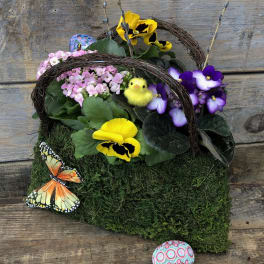 Basket arrangement with yellow and purple pansies, pink flowers, and decorative butterflies