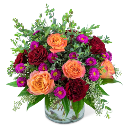 Orange and red roses with purple daisies in a glass vase