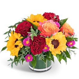 Mixed bouquet of red roses, sunflowers, and pink daisies in a glass vase