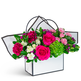 Pink and white floral arrangement in a white handled gift bag