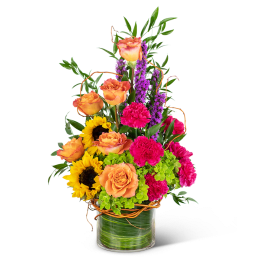 Mixed bouquet with orange roses, sunflowers, pink carnations, and purple spikes in a glass vase