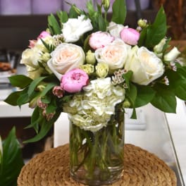 Glass vase arrangement with white hydrangeas, blush roses, and pink blooms with lush foliage
