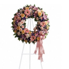 Circular floral wreath on a stand with pink and peach flowers and a ribbon