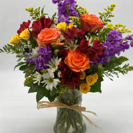 Mixed bouquet of roses, purple stock, and white daisies in a glass vase