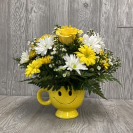 Yellow and white flowers arranged in a yellow smiley-face mug