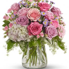 Pink and lavender roses in a glass vase with small purple flowers