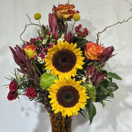 Sunflowers and roses arranged in a tall amber glass vase