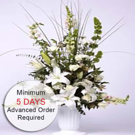 Tall white floral arrangement with lilies and snapdragons in a white urn-style vase