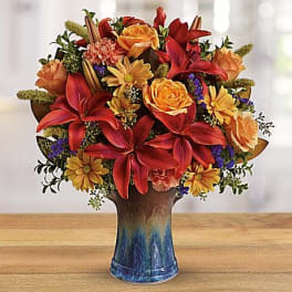 Mixed bouquet of red and orange flowers in a blue vase
