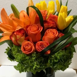 Orange roses and yellow tulips arranged in a glass vase