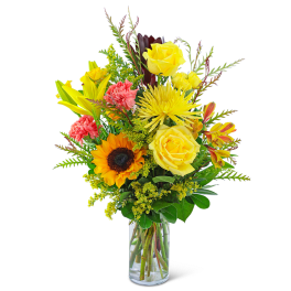 Mixed bouquet of yellow roses, sunflower, lilies, and carnations in a glass vase