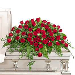 Red rose casket spray with trailing greenery on a white coffin