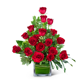 Red roses arranged in a square glass vase with green foliage