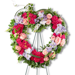 Heart-shaped floral wreath with pink roses and carnations on a stand