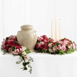 Pink and red rose arrangement around a beige urn with three taper candles