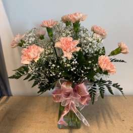 Pink carnations in a glass vase with baby's breath and a pink ribbon