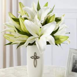 White lilies arranged in a tall white vase with a cross emblem