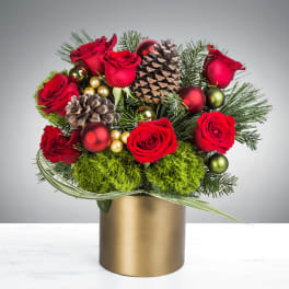 Red rose and evergreen holiday arrangement with pinecones and ornaments in a gold vase