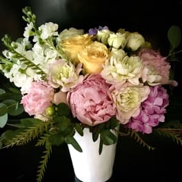 Pastel arrangement of pink peonies, yellow roses and white flowers in a white vase