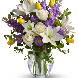 White lilies, roses, purple flowers, and yellow tulips in a glass vase