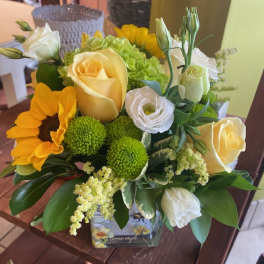 Bouquet of yellow roses, sunflowers, and white blooms in a glass vase