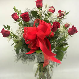 Red roses in a clear glass vase with a large red bow